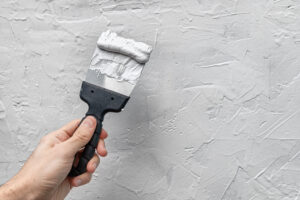 Applying putty or drywall plaster to a vertical wall in a renovated house with a spatula or trowel.